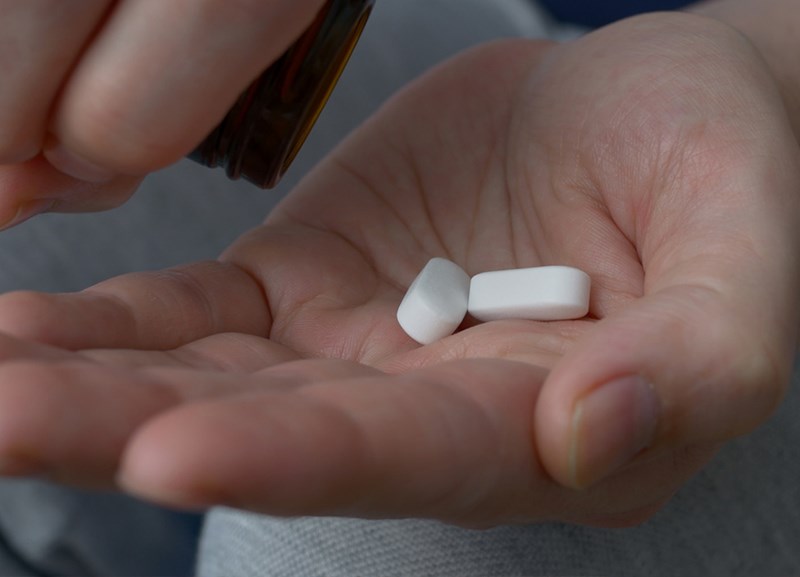 Nærbilde av hånd med to smertestillende tabletter
